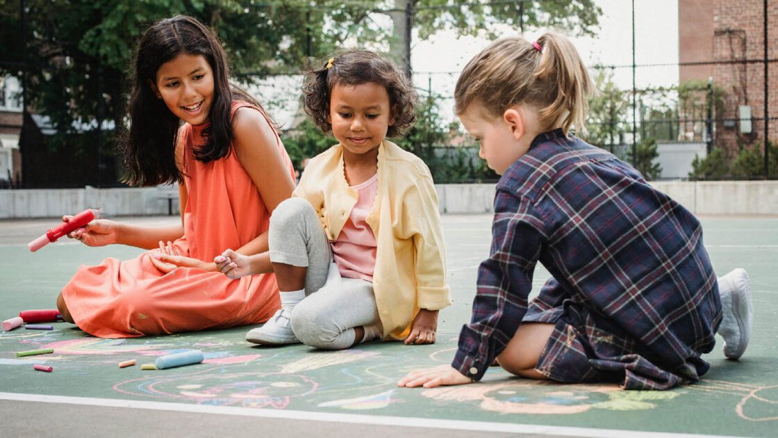 Three girls drawing with chalk on an outdoor surface.