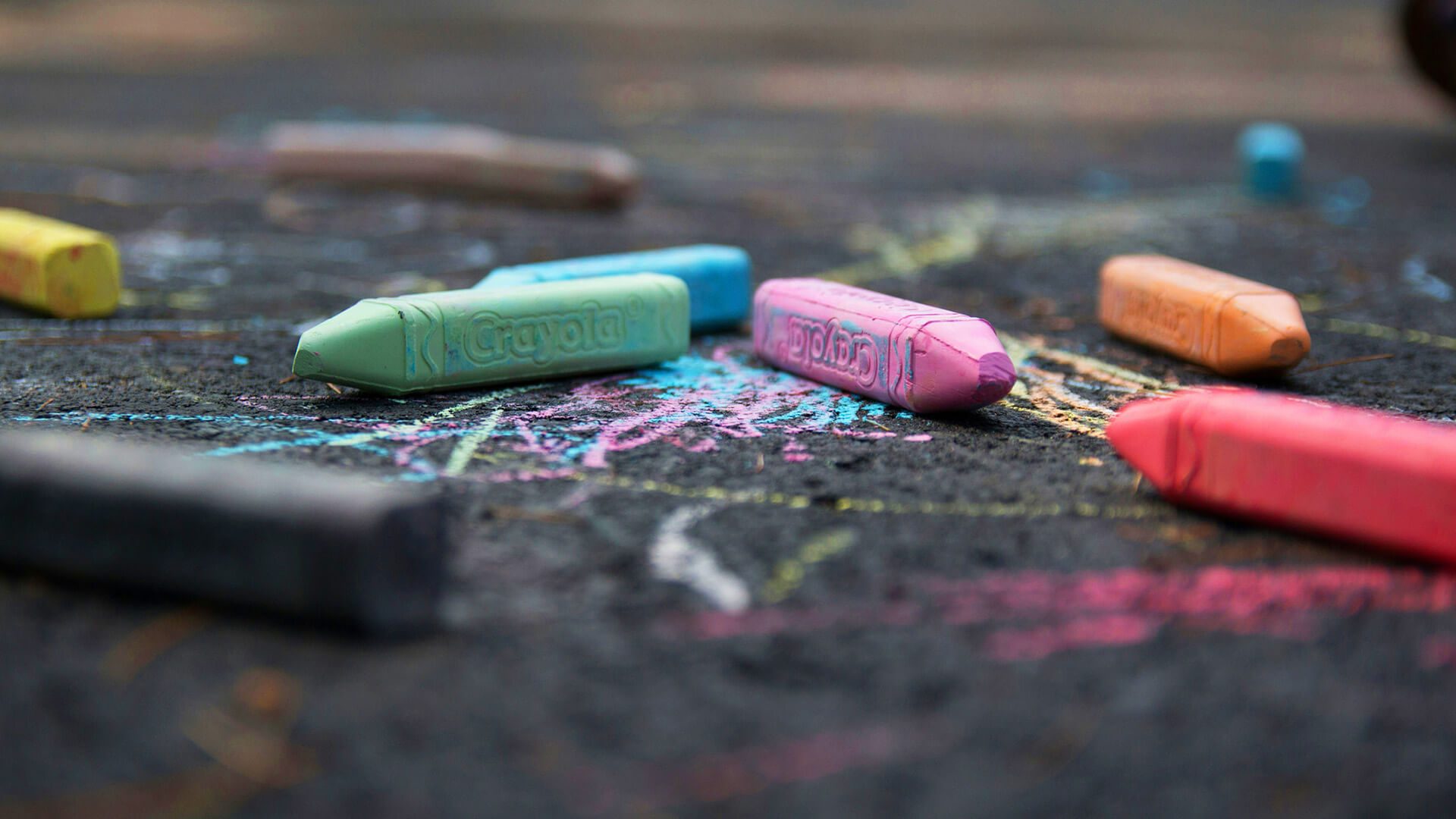 Close-up of colorful Crayola sidewalk chalk and drawings on dark pavement.