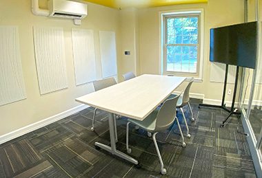 Conference room with a table, chairs, TV on a stand, yellow ceiling and glass wall.
