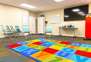 Bright, colorful space with chairs, alphabet rug, TV, and white cabinets.