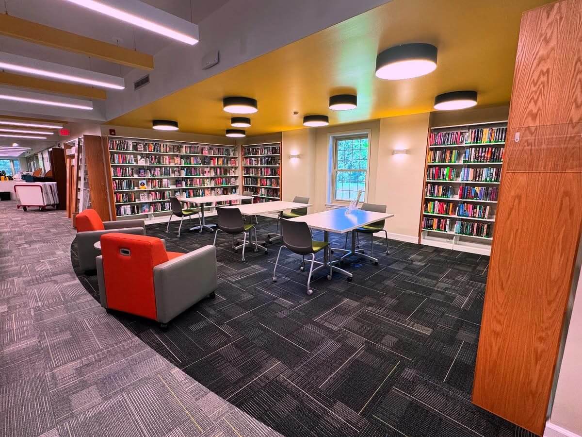 Library interior with books, tables, chairs and orange armchairs.
