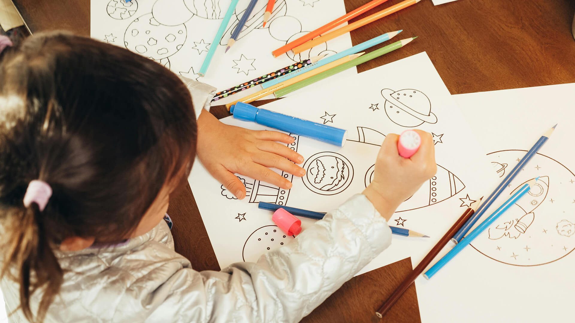 A child coloring space themed pages on a wooden table.