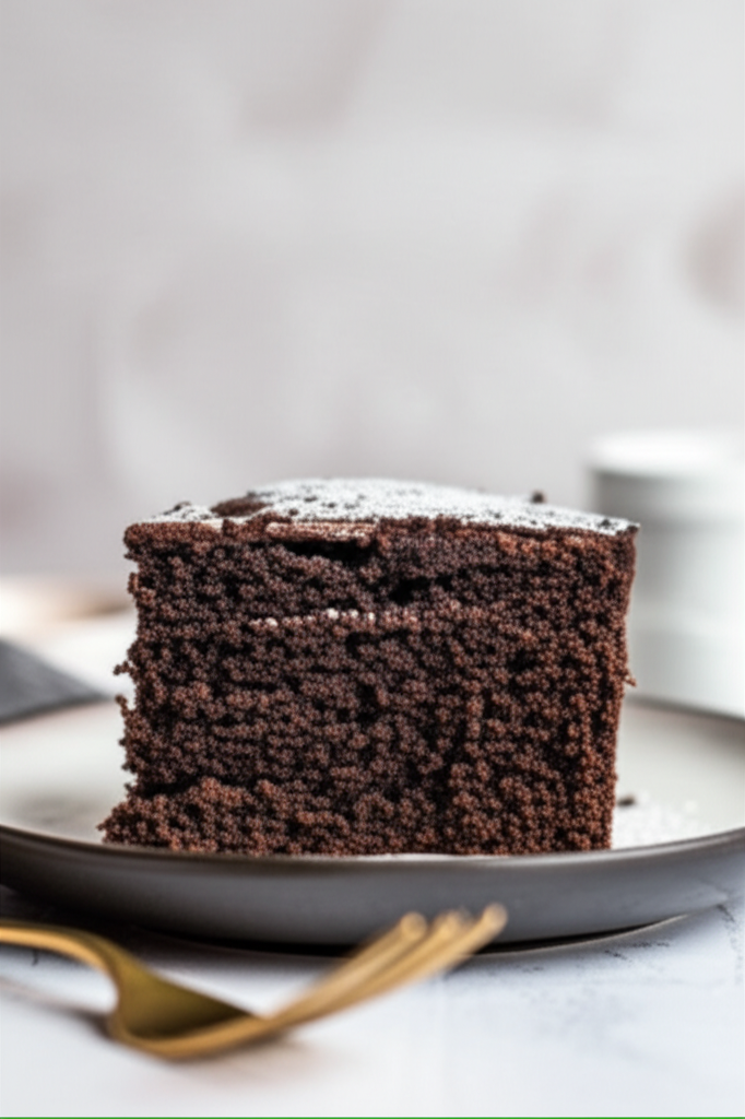 Slice of dark chocolate cake with powdered sugar on a plate, showing a moist, porous texture.