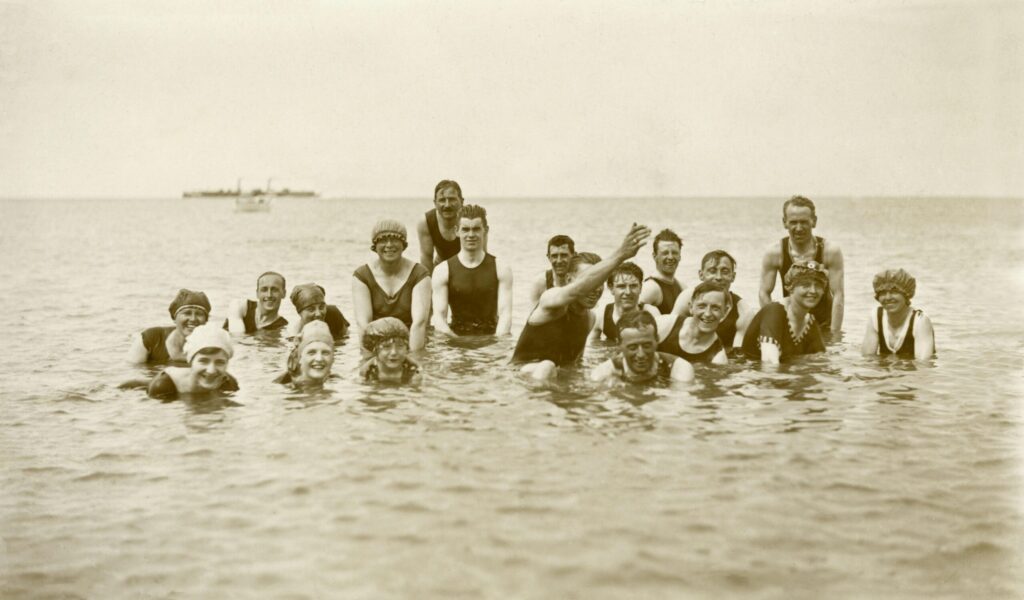 Vintage photo of a group of young people in old fashioned bathing suits having fun in the sea