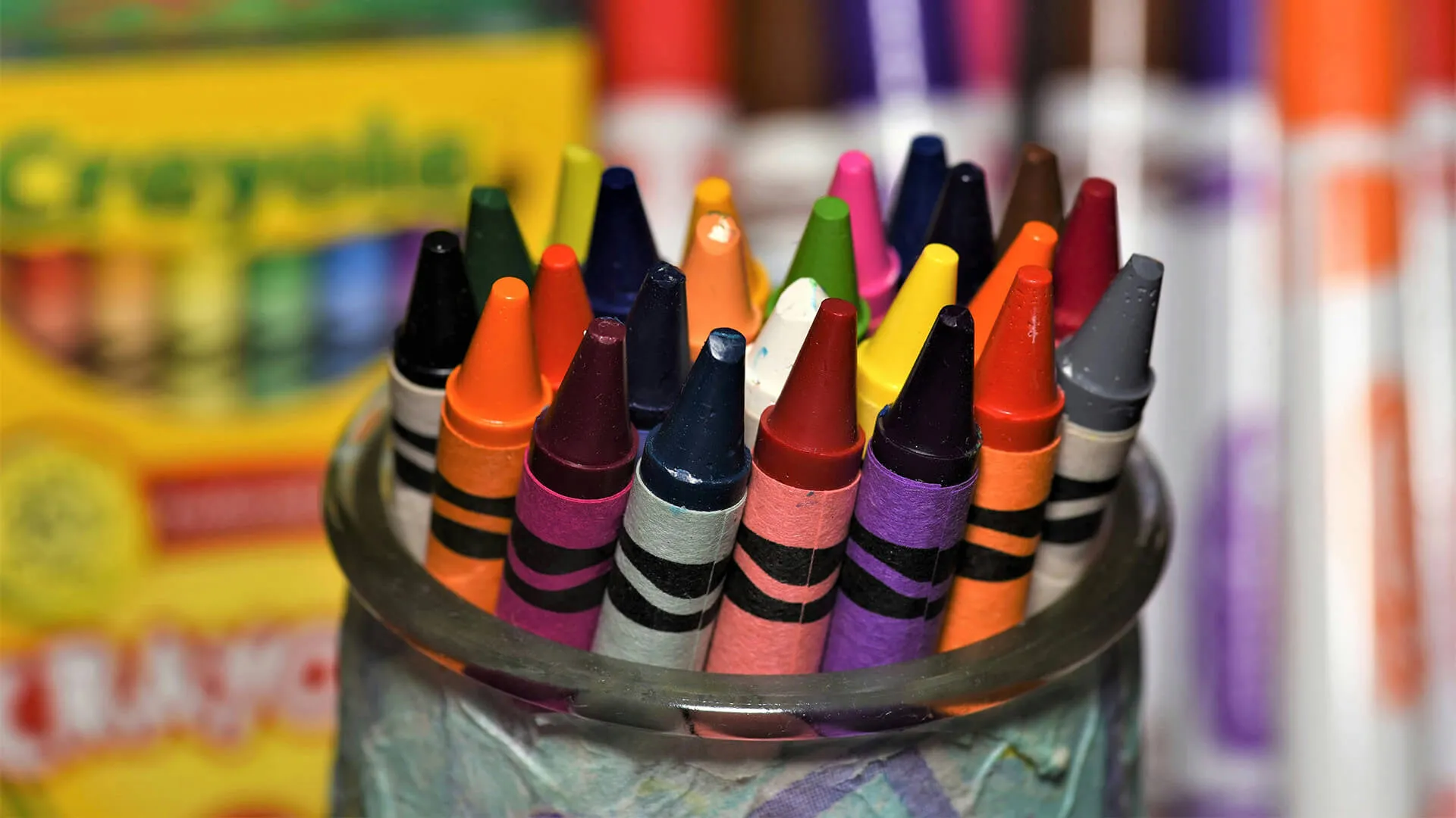Colorful Crayola crayons with pointed tips standing upright in a clear glass.