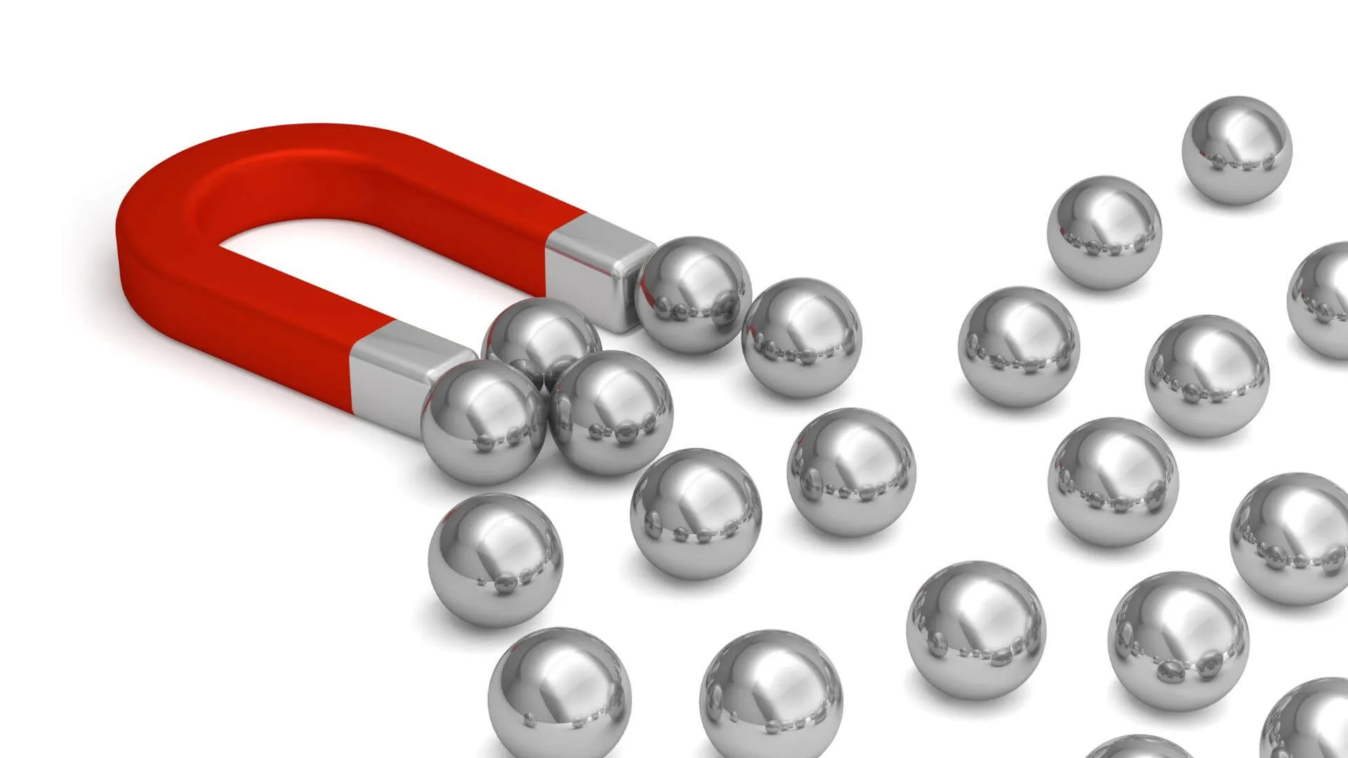A red horseshoe magnet pulls shiny silver metallic spheres, some attached, many scattered on white table top.