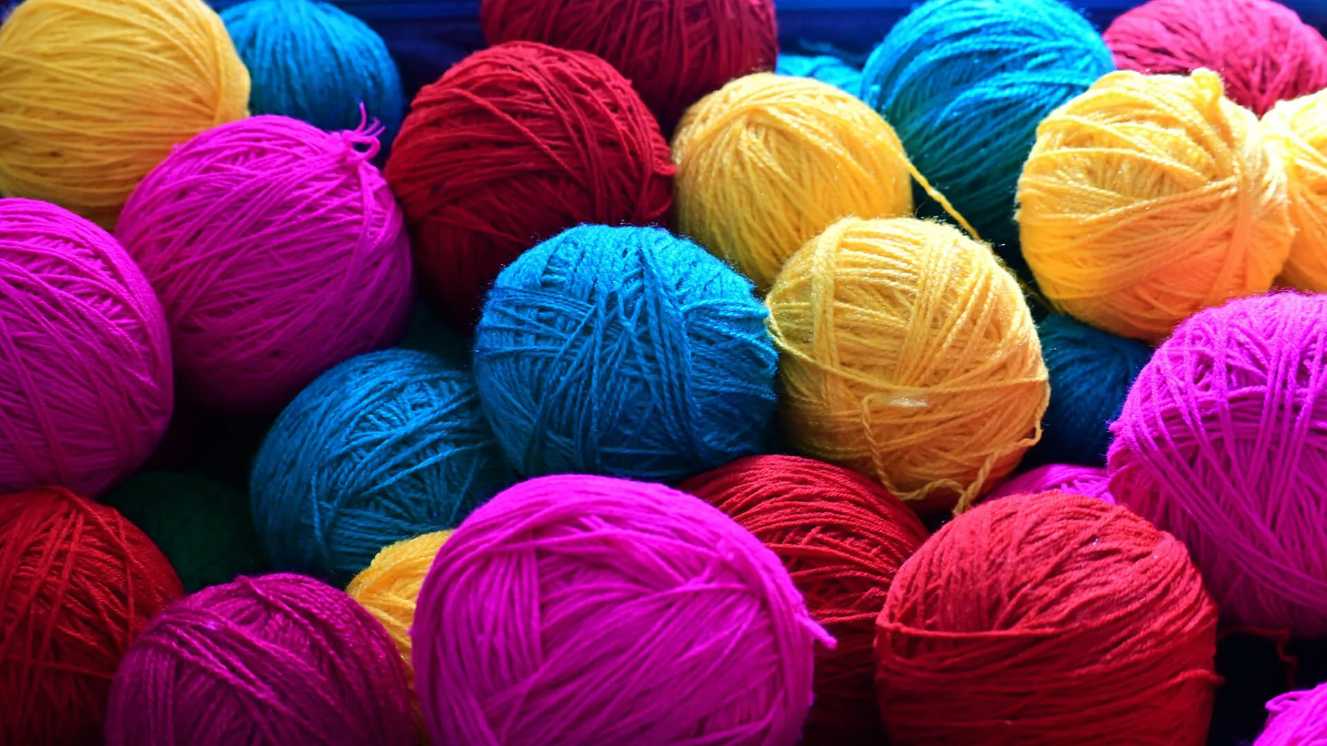 Vibrant pile of yarn balls: yellow, red, blue, and magenta threads tightly wound.