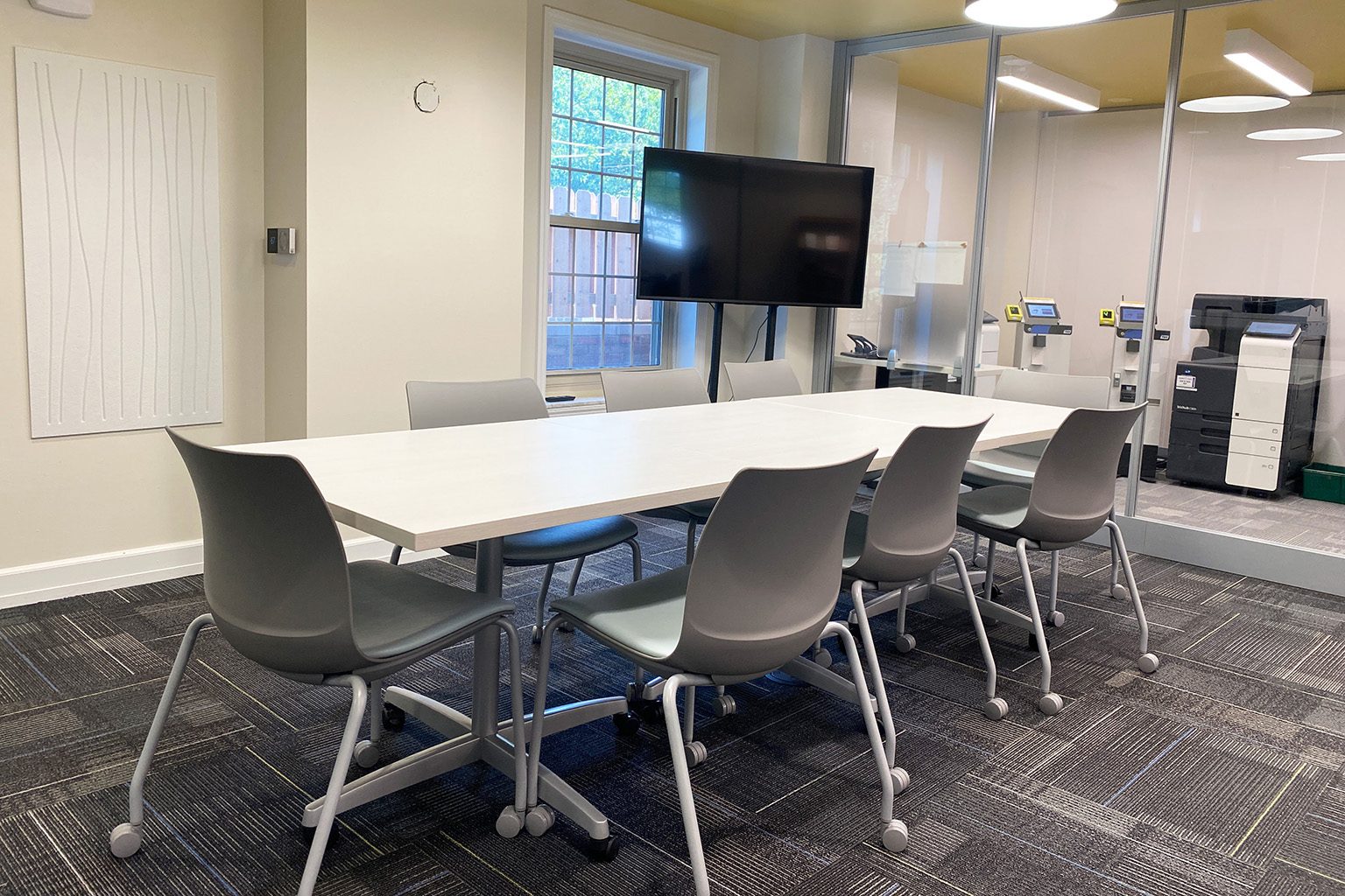 Modern meeting room with a long white table, gray chairs, a large TV.