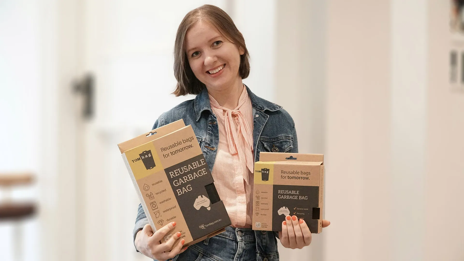 Smiling woman holds two different-sized boxes of 'Reusable Garbage Bag' products.