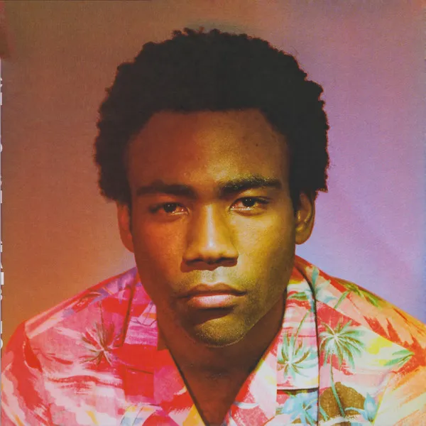 Close-up of Donald Glover with an afro, serious look, wearing a vibrant tropical shirt.