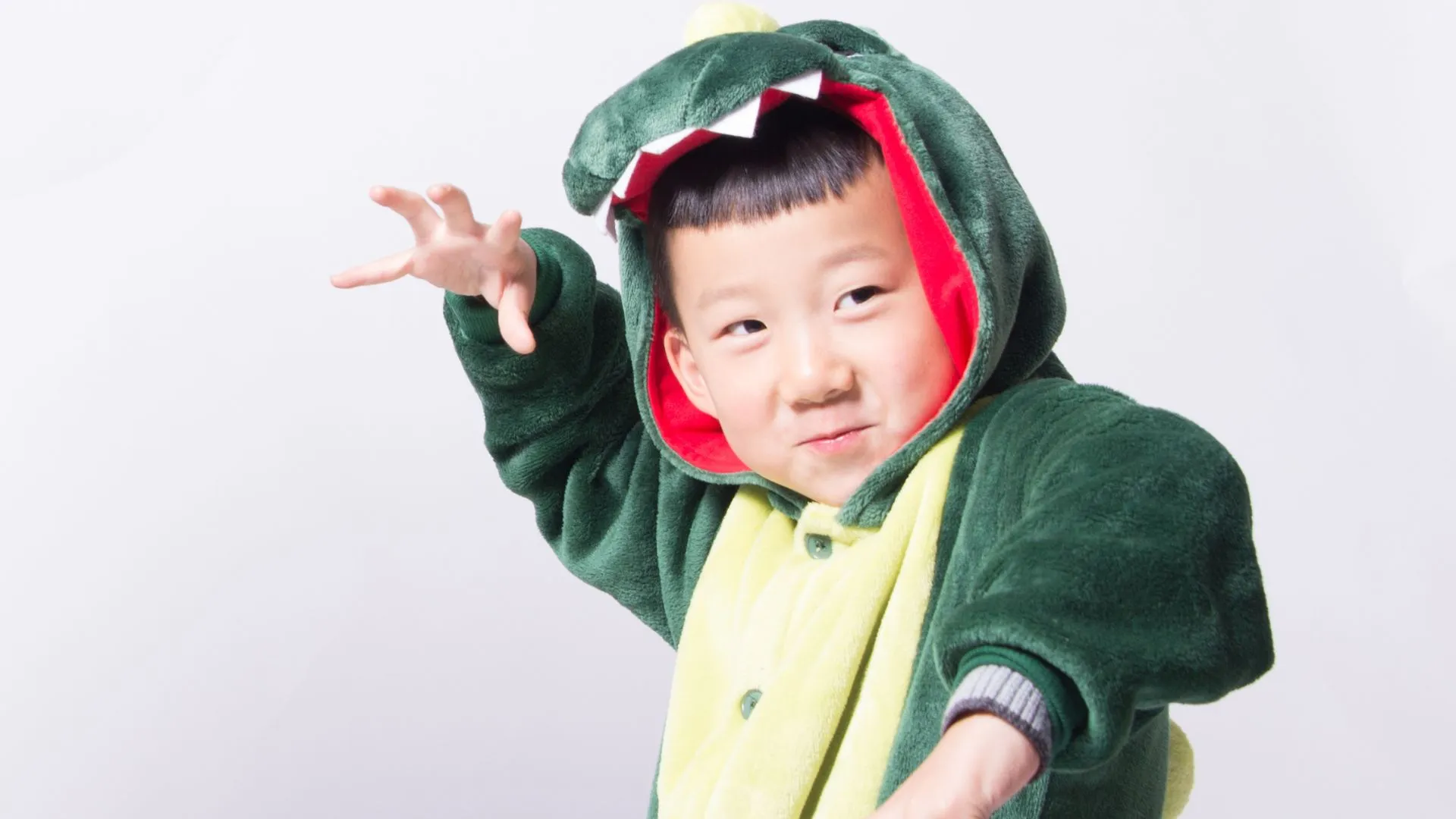 A young child in a green dinosaur costume making a playful claw gesture.