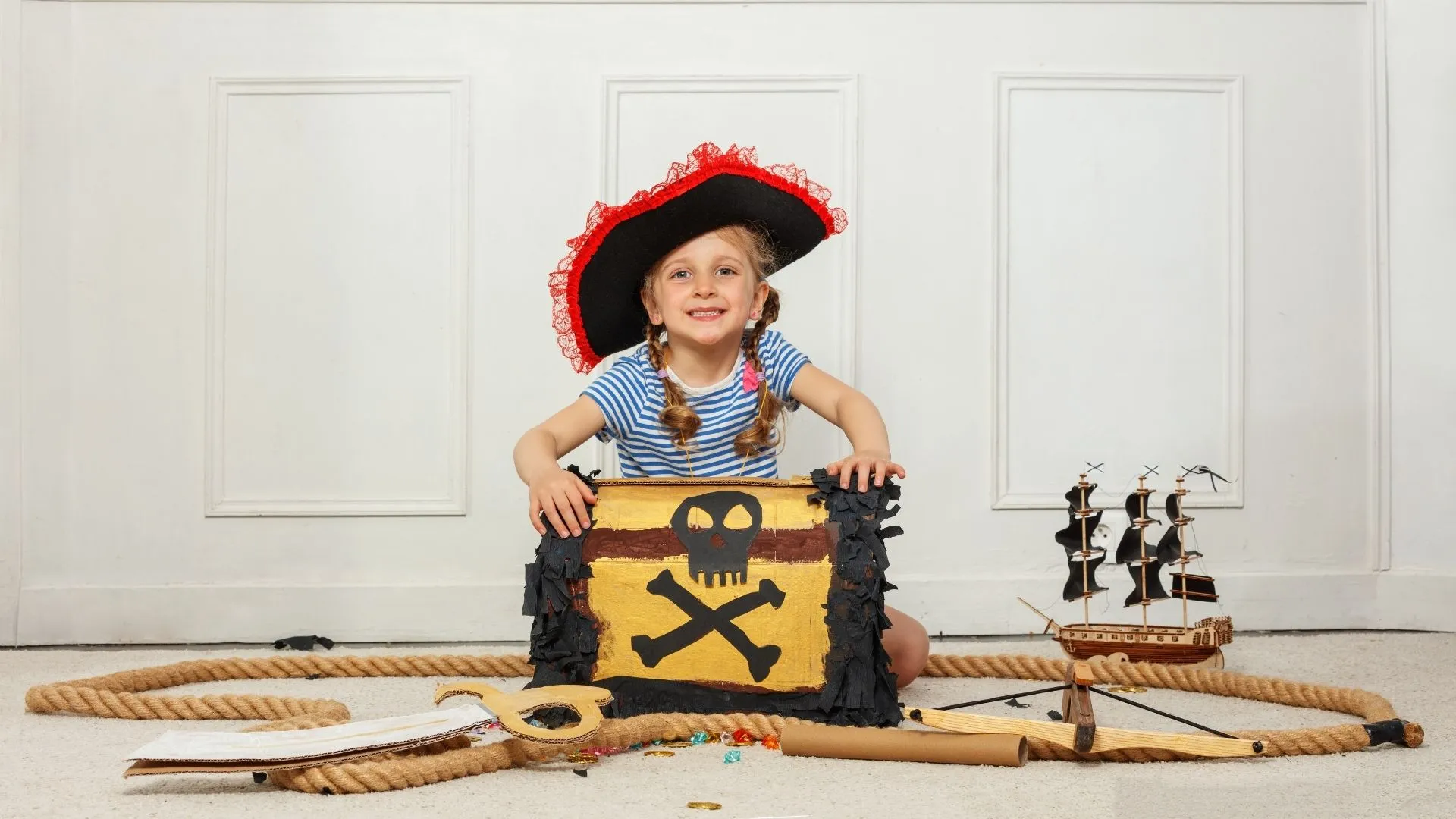 Smiling pirate girl behind a DIY skull & crossbones treasure chest, surrounded by themed props.