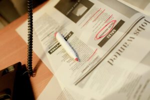 Stack of wanted ads, some cirled with red marker, next to a landline phone in use