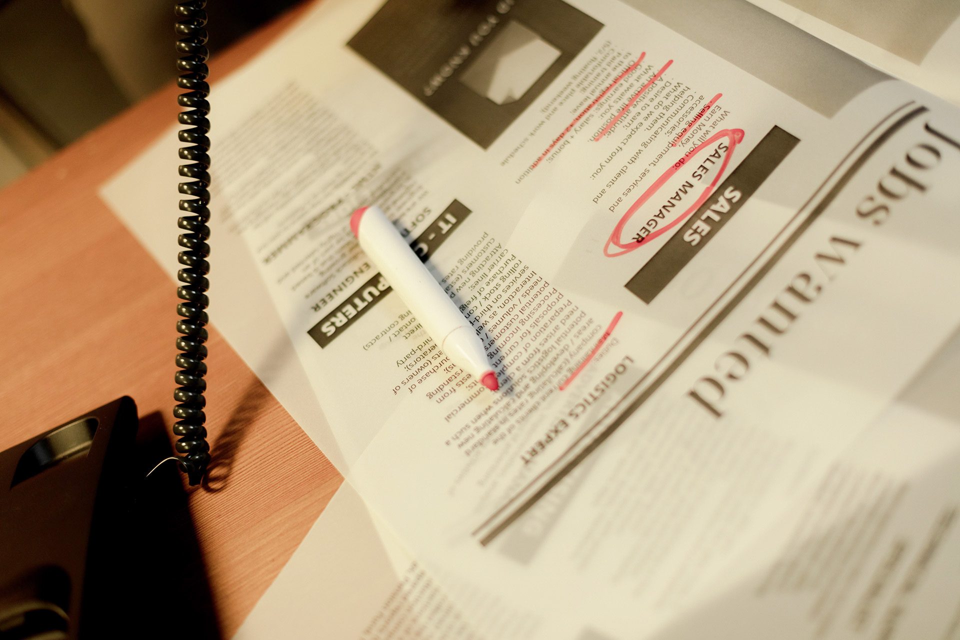 Stack of wanted ads, some cirled with red marker, next to a landline phone in use