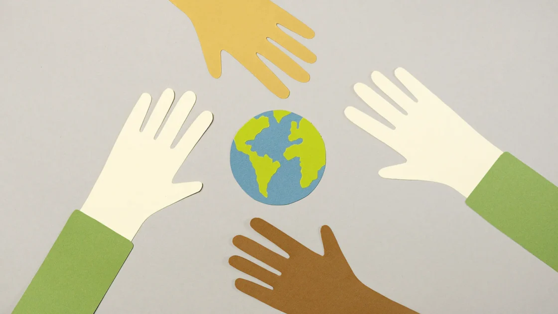 Four paper-cutout hands of different skin tones surrounding a small paper globe.