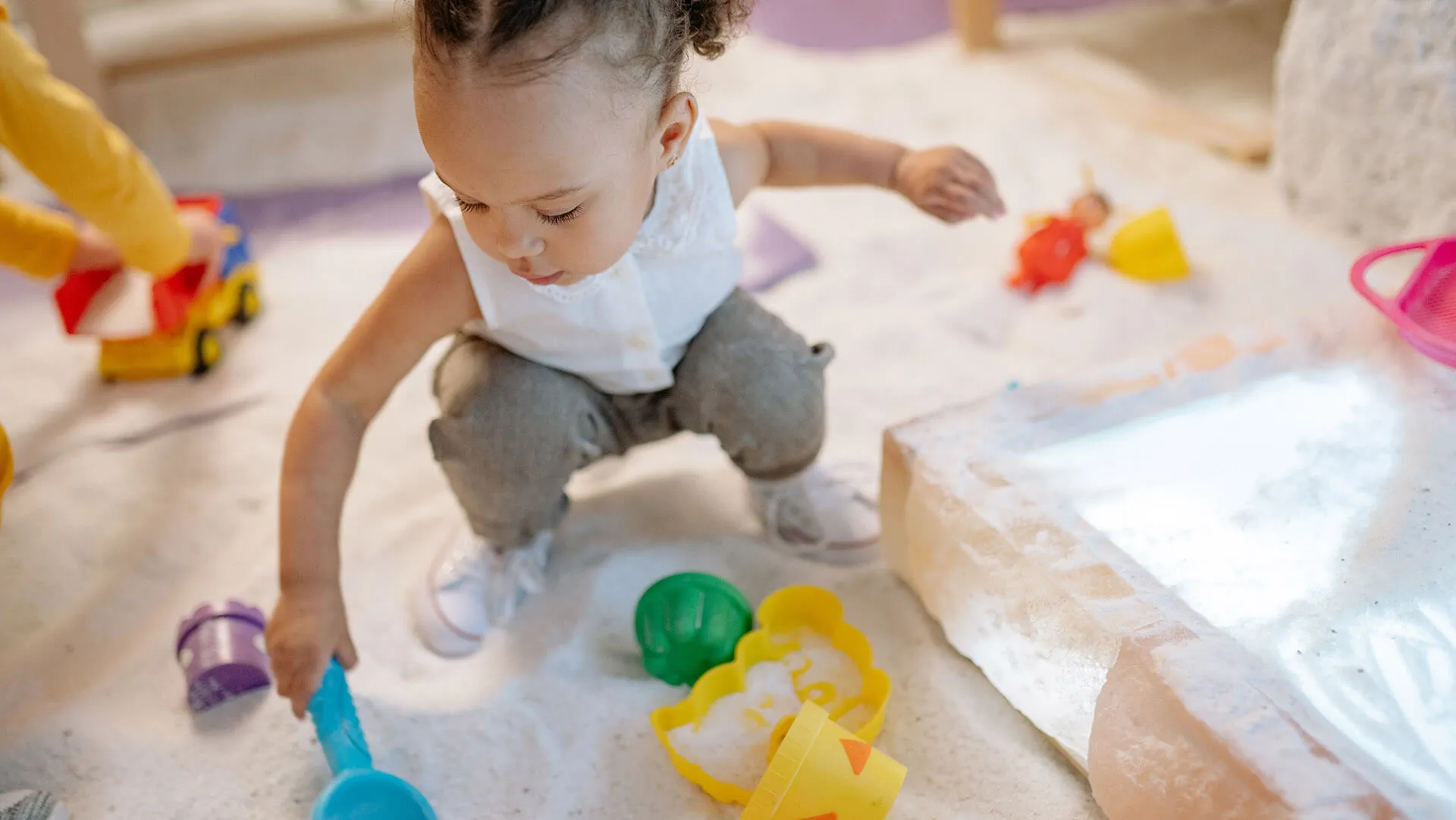A young child playing with beach toys in a sandpit.