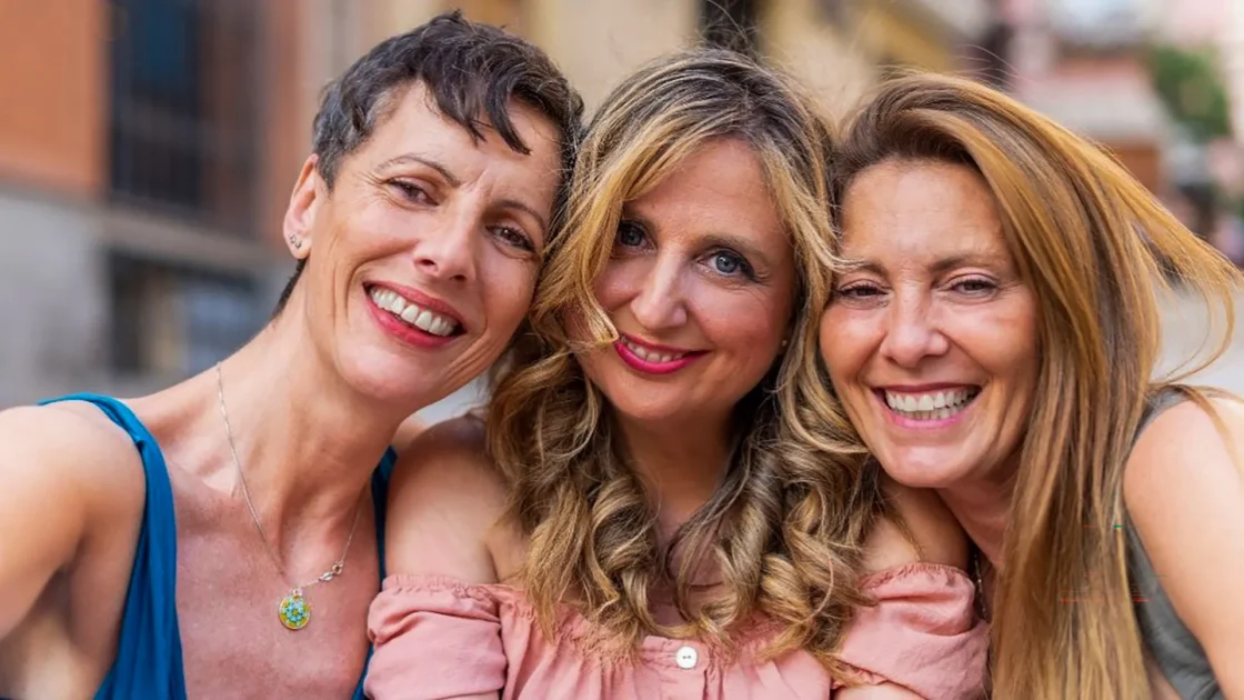Three women smiling together in a close-up selfie outdoors.