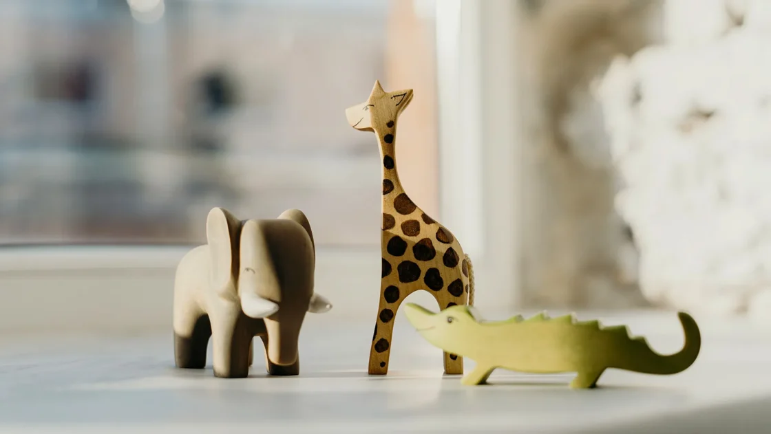 Wooden elephant, giraffe, and crocodile toys sitting on a windowsill.