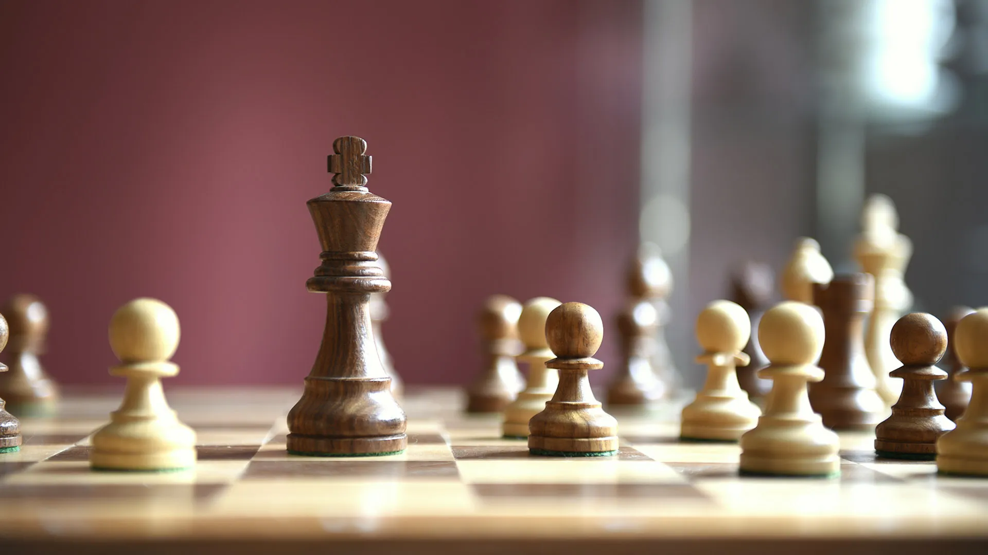 Board level view of a dark wooden chess king standing on a chessboard among several light and dark wooden pawns.