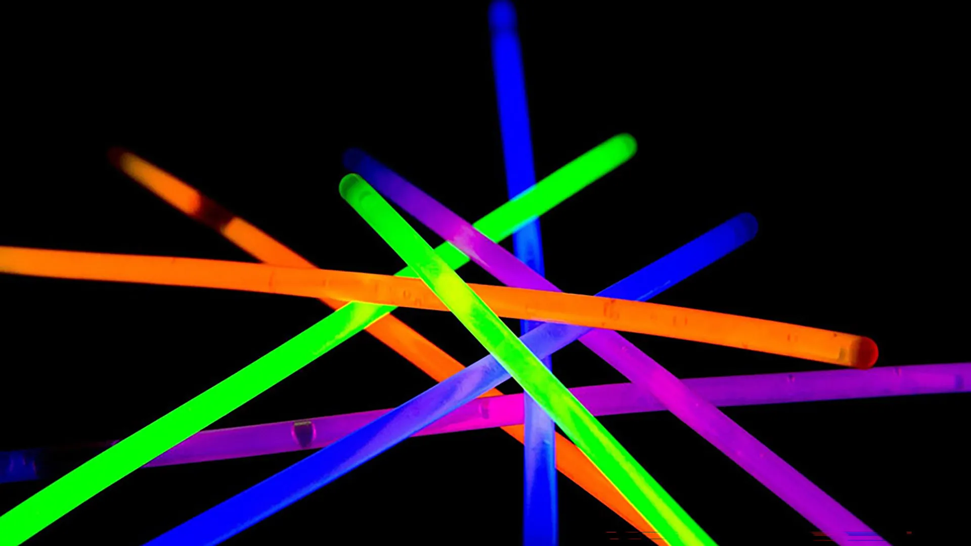 A vibrant pile of glowing neon glow sticks in various colors against a dark background.